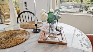 Une table à manger avec un plateau en marbre blanc, un set de table en fibres tressées, une bougie et un vase rempli de fleurs.