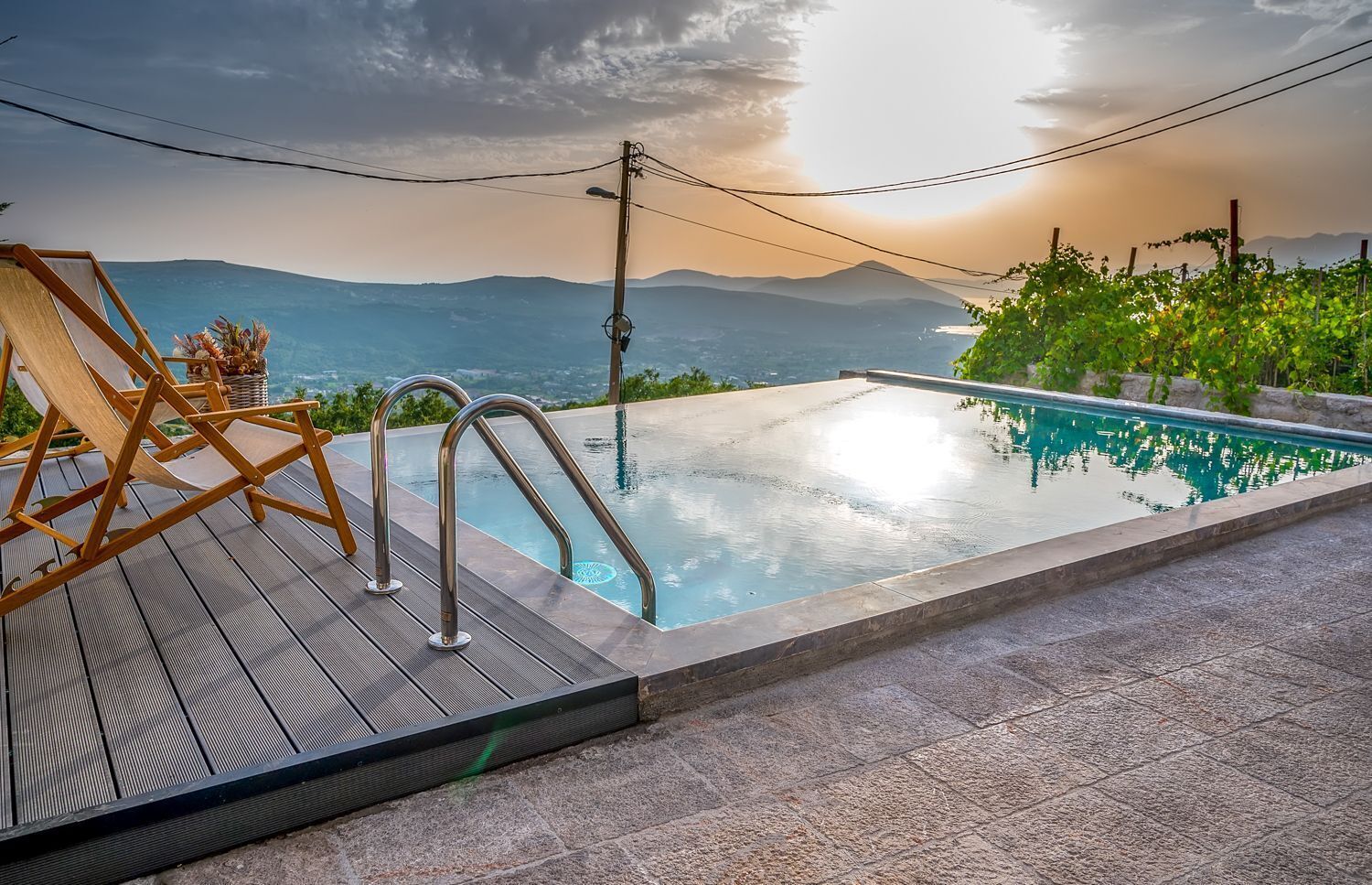 Une piscine avec vue sur les montagnes, une terrasse en bois et une rambarde en métal.