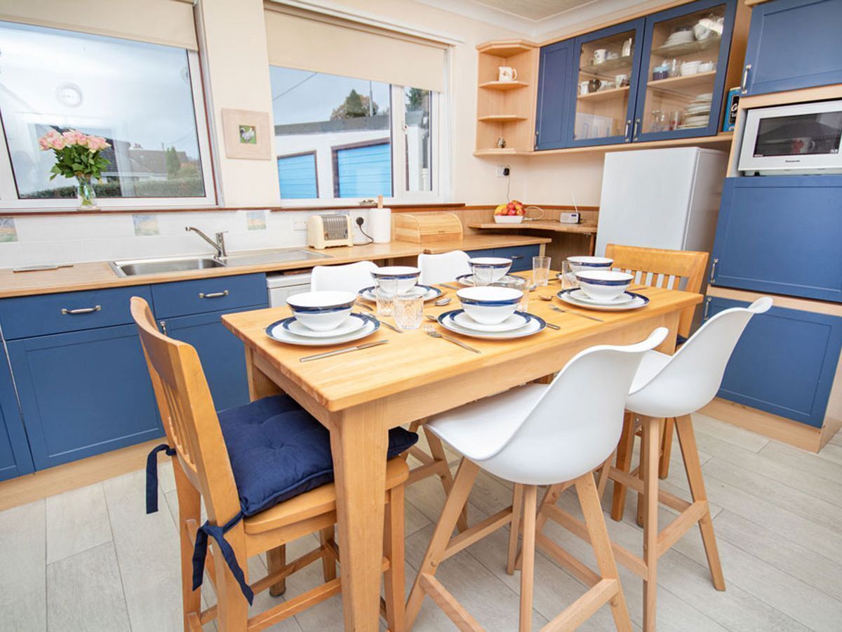 Una cocina moderna con armarios azules, una mesa de comedor de madera dispuesta para cuatro personas y un amplio ventanal que proporciona luz natural.