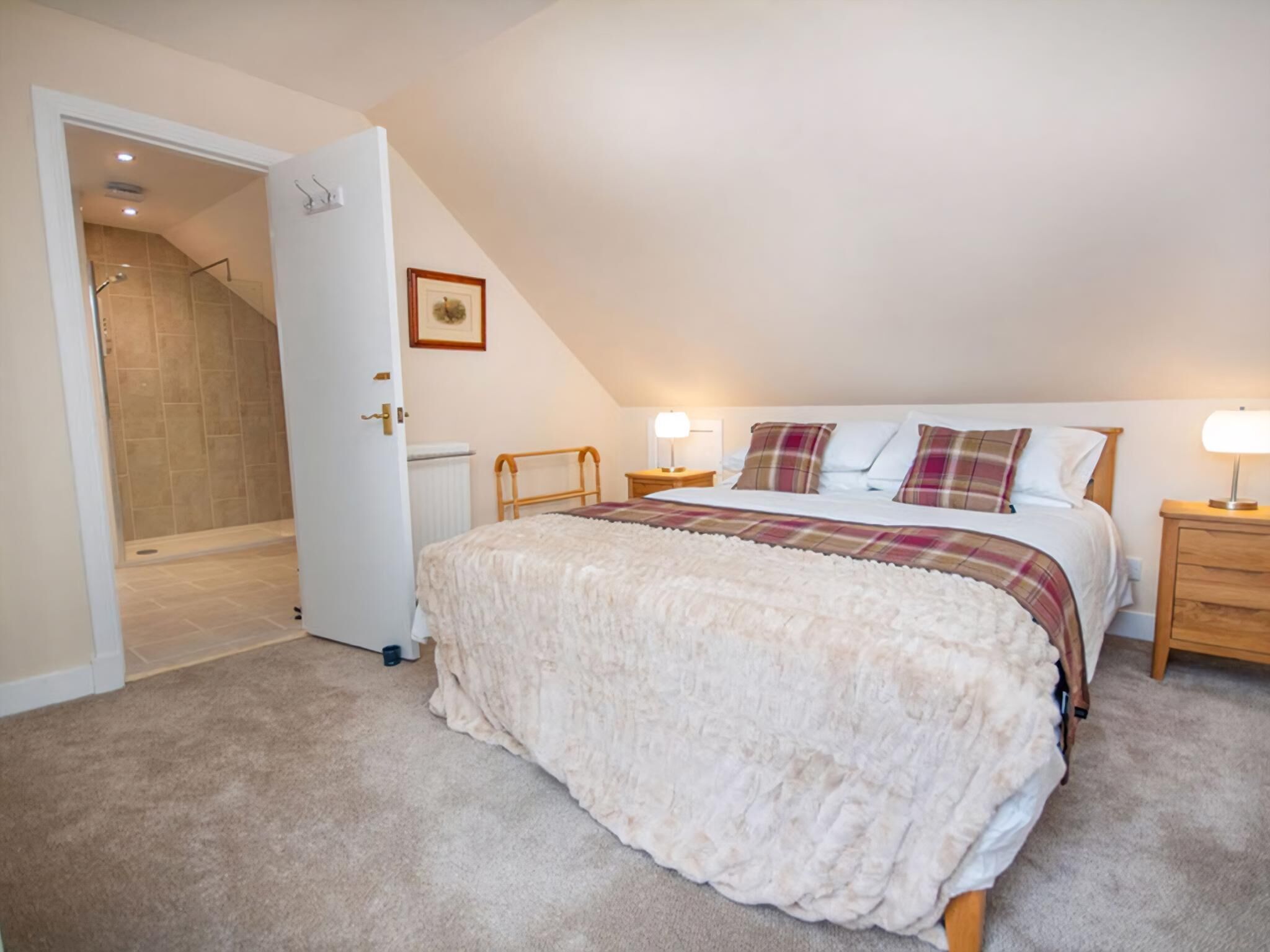 Une chambre à coucher avec un grand lit, une tête de lit en bois, deux tables de chevet avec des lampes, une porte donnant sur une salle de bain et un tableau encadré au mur.
