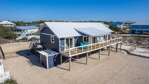 Una casa sulla spiaggia con una veranda coperta, un piccolo spazio relax all'aperto e una scala che conduce all'edificio principale.