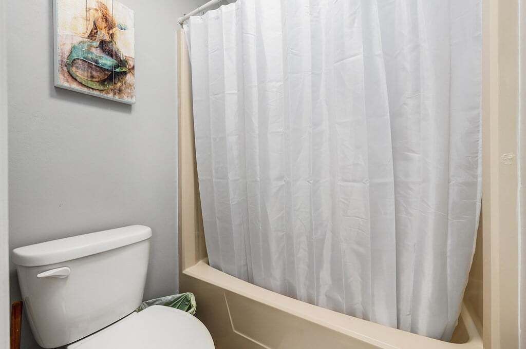 A bathroom with a white toilet, a shower curtain, and a painting on the wall.