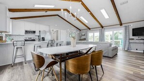 Un'ampia zona giorno con tavolo da pranzo, sedie in legno, divano e cucina sullo sfondo.
