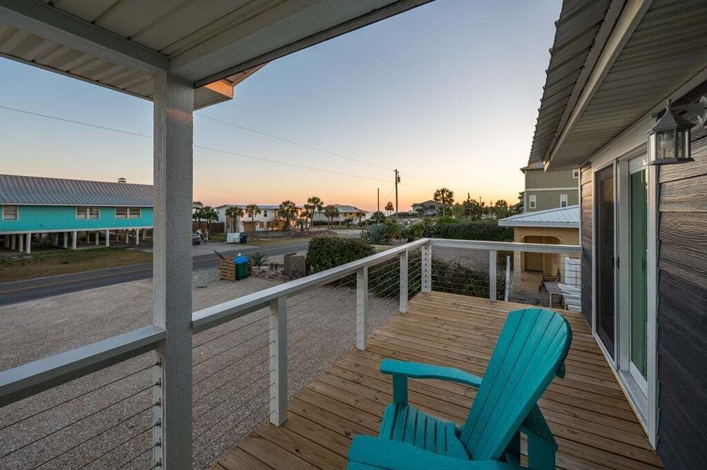 A wooden deck with a chair, a covered area, and a view of a street with houses.