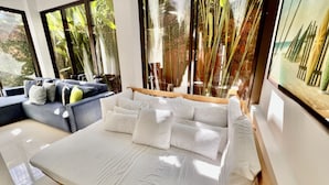 A modern bedroom with a large bed, a sofa, and a view of bamboo plants through the windows. - Huge Private Home - Exclusive Beach Access and Breathtaking Rooftop Sunset Views (Jaco beach)
