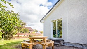 A wooden picnic table with benches in a backyard with a house in the background.
