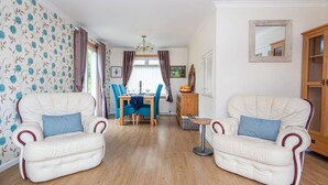 A living room with two white leather sofas, a dining table with blue chairs, and a wooden cabinet.