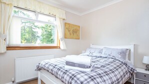 A bedroom with a bed, a nightstand, a window with curtains, a radiator, and a wall-mounted artwork.