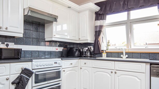 A kitchen with white cabinets, a stove, an oven, a microwave, and a window with curtains.