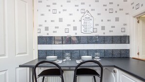 A kitchen with a tiled backsplash, a sign indicating operating hours, and two bar stools.