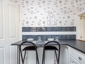 A kitchen with a tiled backsplash, a sign indicating operating hours, and two bar stools.