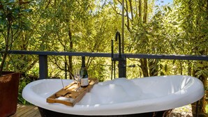 Ein Whirlpool auf einer Holzterrasse mit Metallgeländer, umgeben von üppigem Grün.