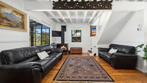 Ein Wohnzimmer mit zwei Ledersofas, einem gemusterten Teppich, einem Kamin und einem großen Fenster mit einem Gemälde.