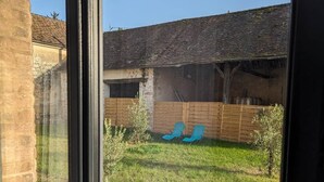 A view through a glass door of a backyard with a grassy area, two blue lounge chairs, and a wooden fence.