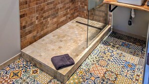 A bathroom with a shower area featuring a glass door, a sink with a wooden countertop, and a tiled floor with a mix of patterns.