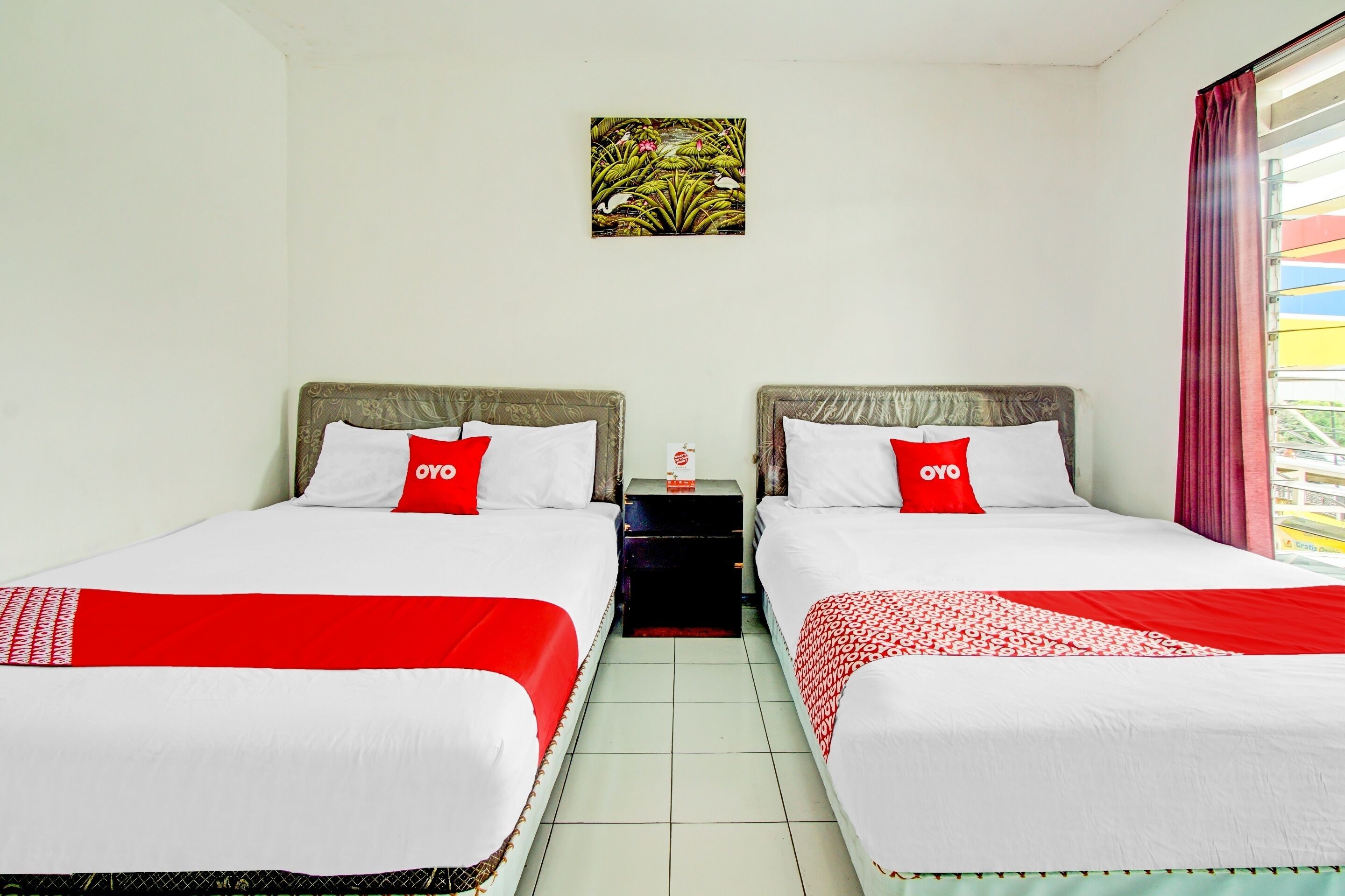 Habitación de hotel con dos camas, cada una con una colcha y almohadas rojas y blancas con el sello “OYO”. Una pequeña mesa con una caja de pañuelos se encuentra entre las camas.