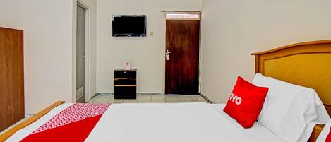 A hotel room with a bed, a wooden headboard, a red and white bedspread, a red pillow with the word "YOYO", a television mounted on the wall, and a door leading to another room.
