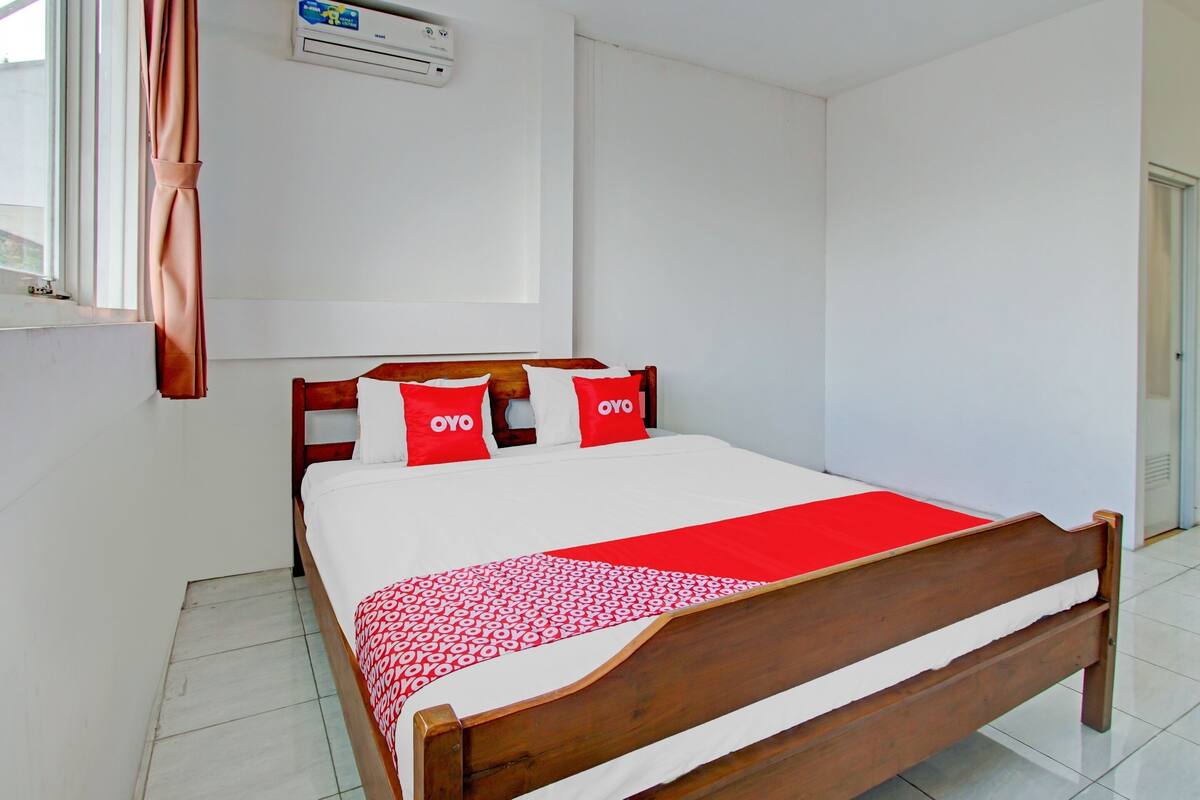 A neatly made bed with a wooden frame, white bedding, and red accents.