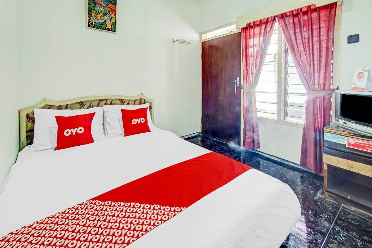 A hotel room with a bed, a TV, and a window with curtains.