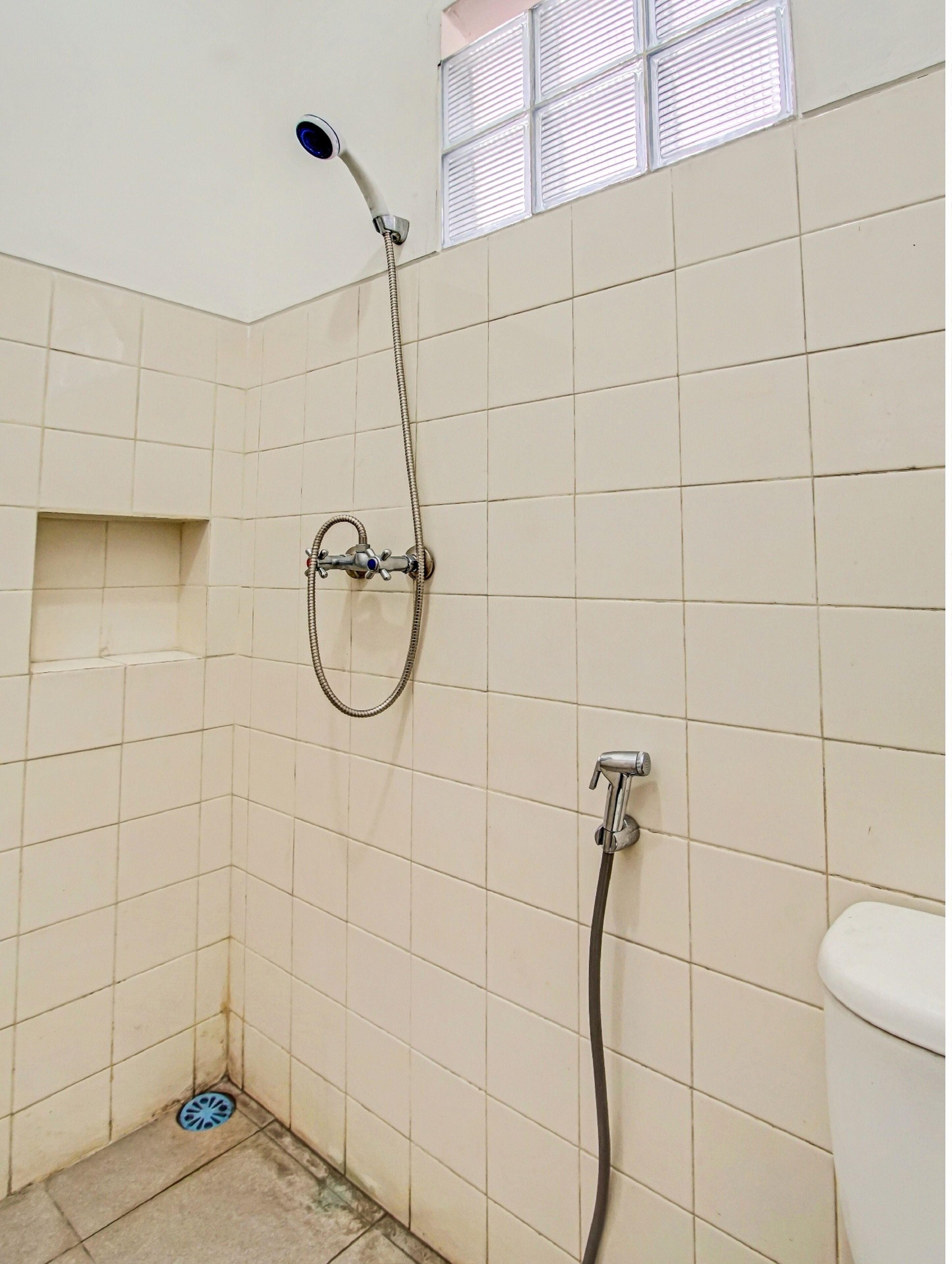 A small, tiled bathroom with a shower, a toilet, and a window with blinds.