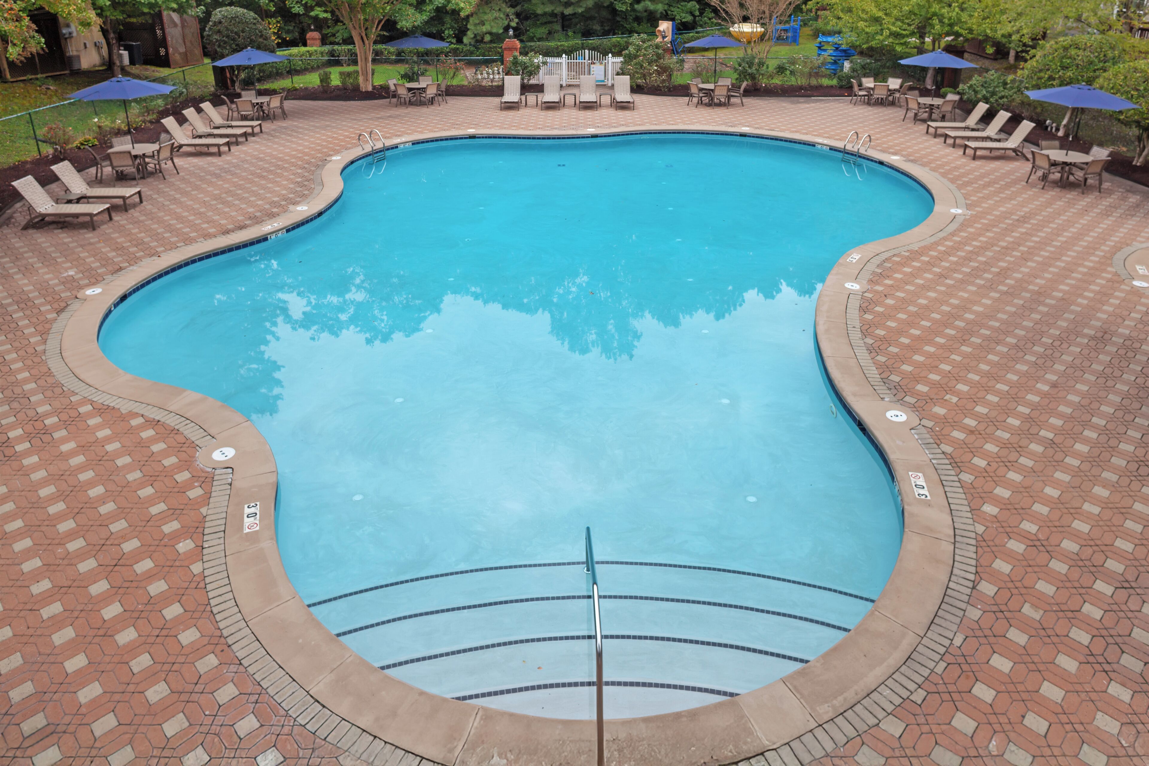 Una piscina con solárium de ladrillo, sillas de descanso y sombrillas.