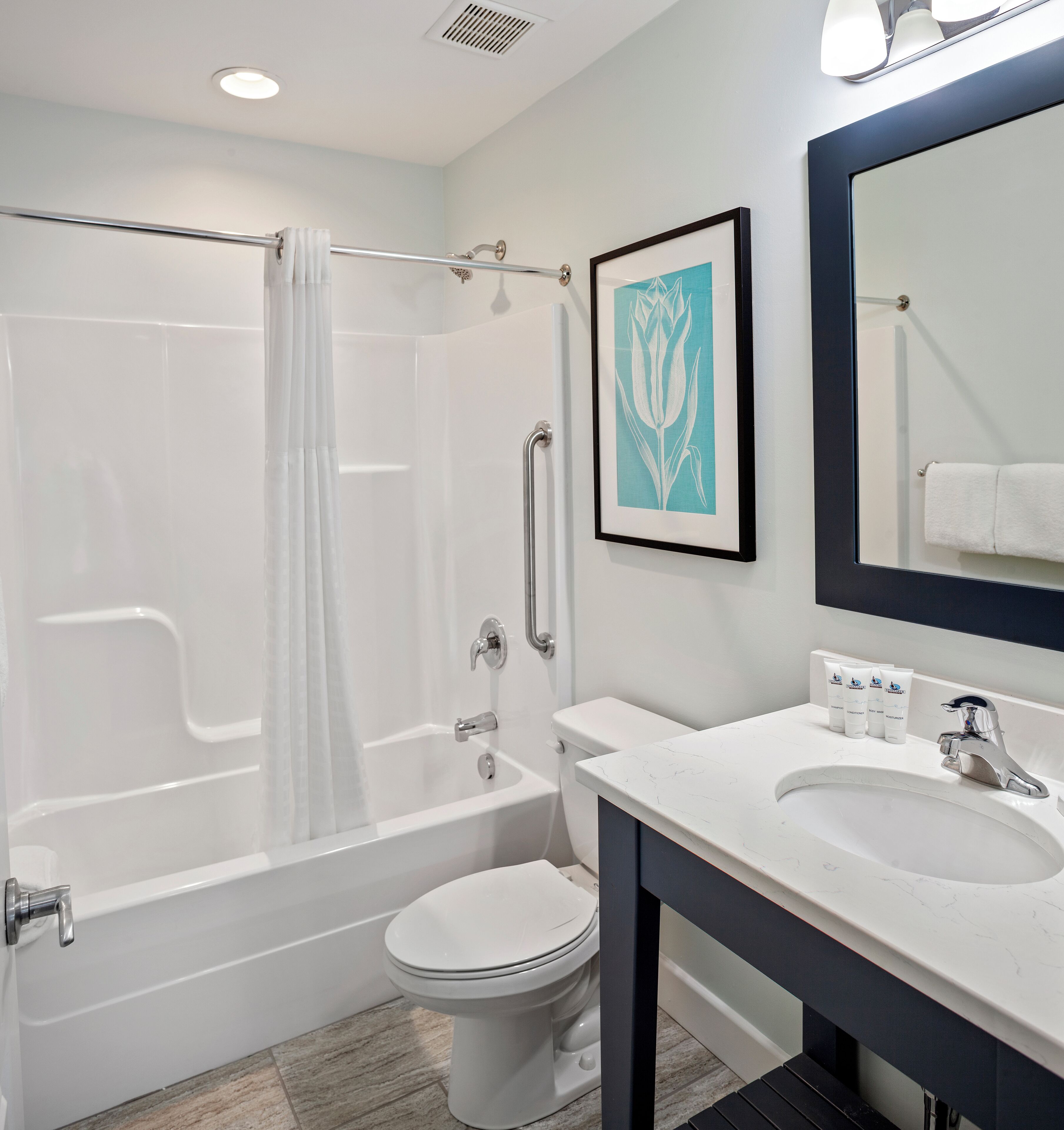 A modern bathroom with a bathtub, toilet, sink, and a framed artwork on the wall.