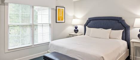 A neatly arranged bedroom with a large bed, a bench, two bedside tables, and a window with blinds.