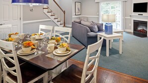 Un comedor con una mesa de madera dispuesta para una comida, sillas blancas y una lámpara colgante azul.