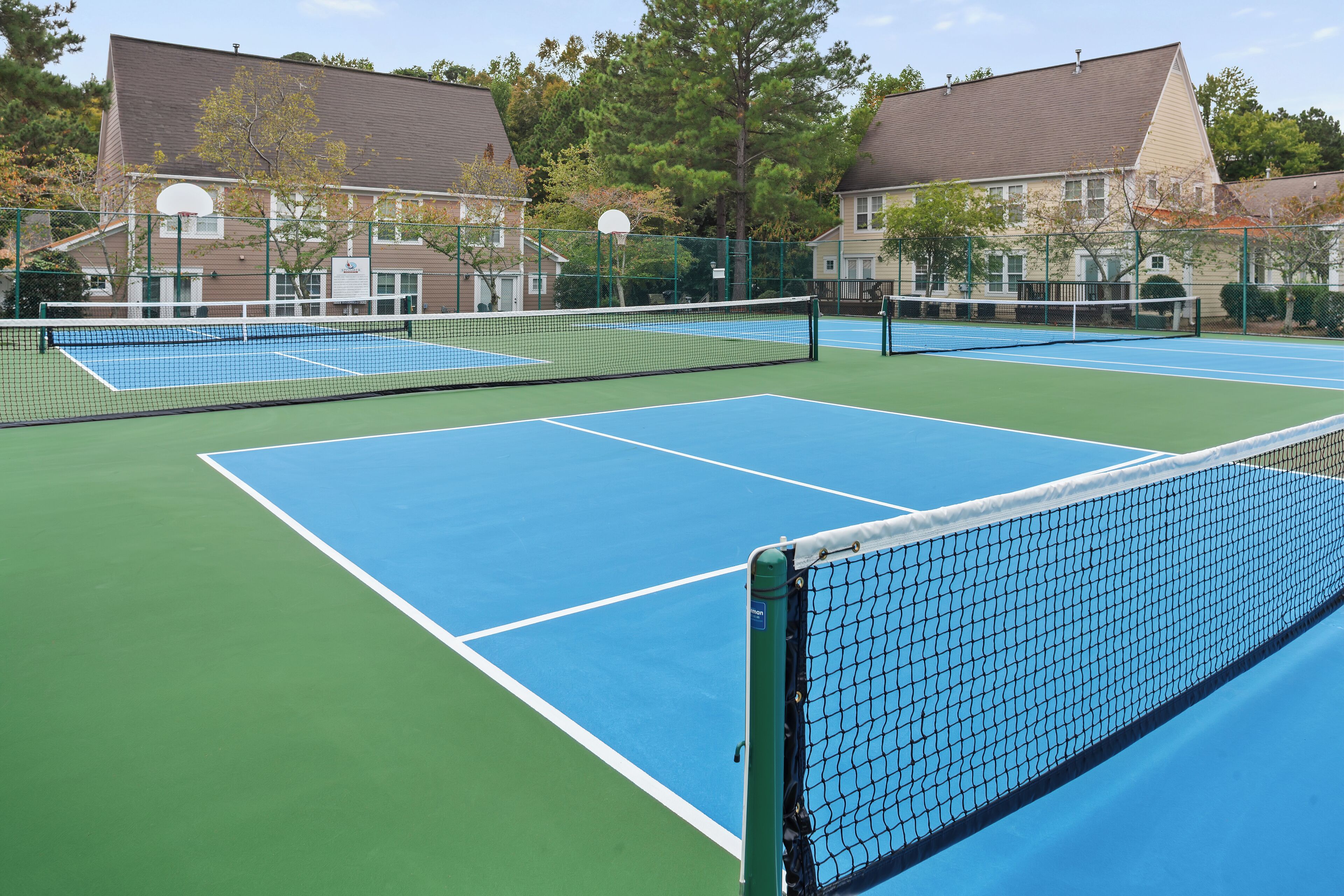 Cancha de tenis exterior con varias canchas, rodeada de edificios residenciales.