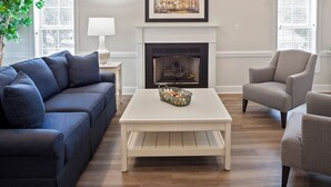Una sala de estar con chimenea, un sofá azul, una mesa de centro blanca y dos sillones.