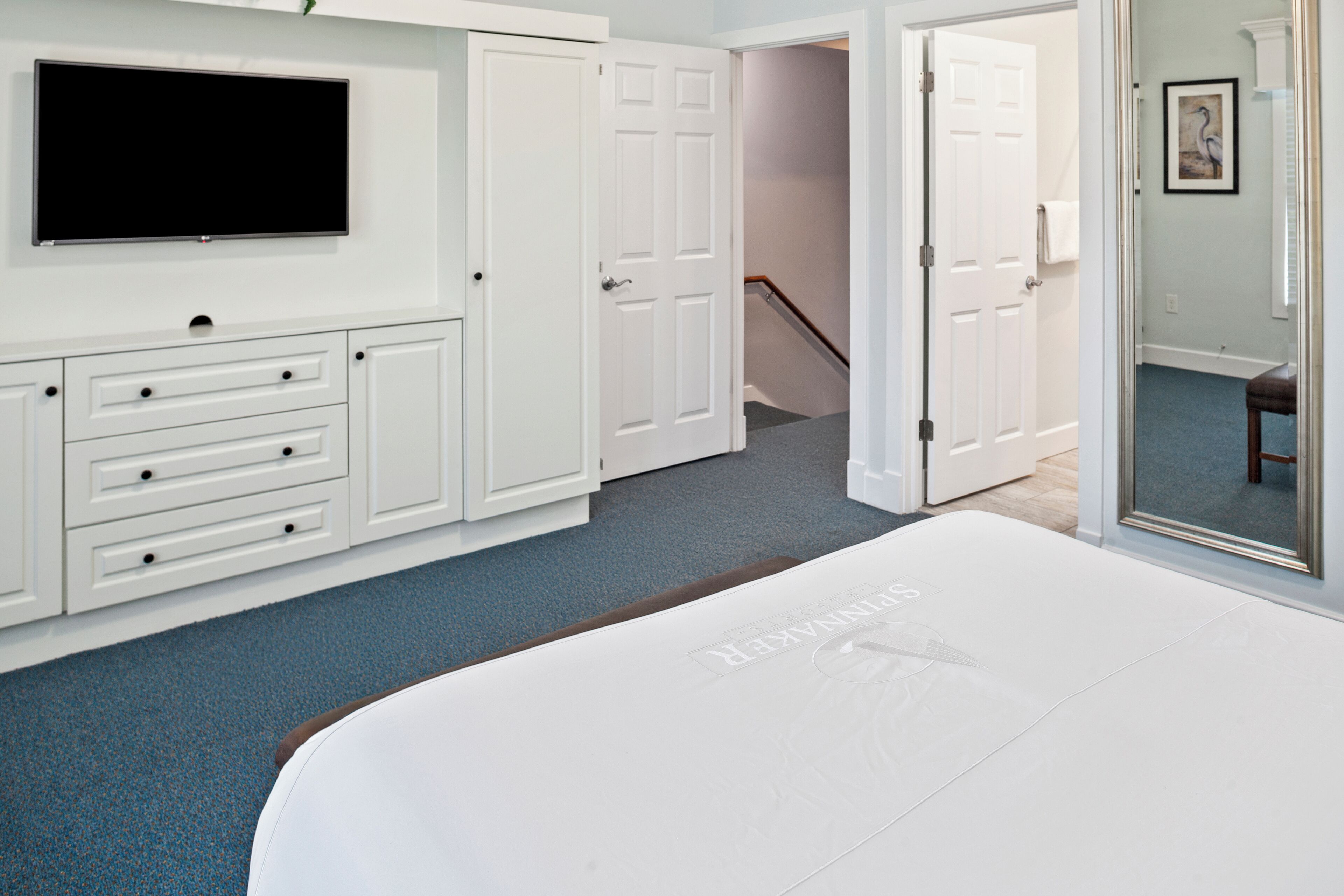 A hotel room with a large bed, a flat-screen TV mounted on the wall, white built-in cabinetry, and a door leading to a staircase.