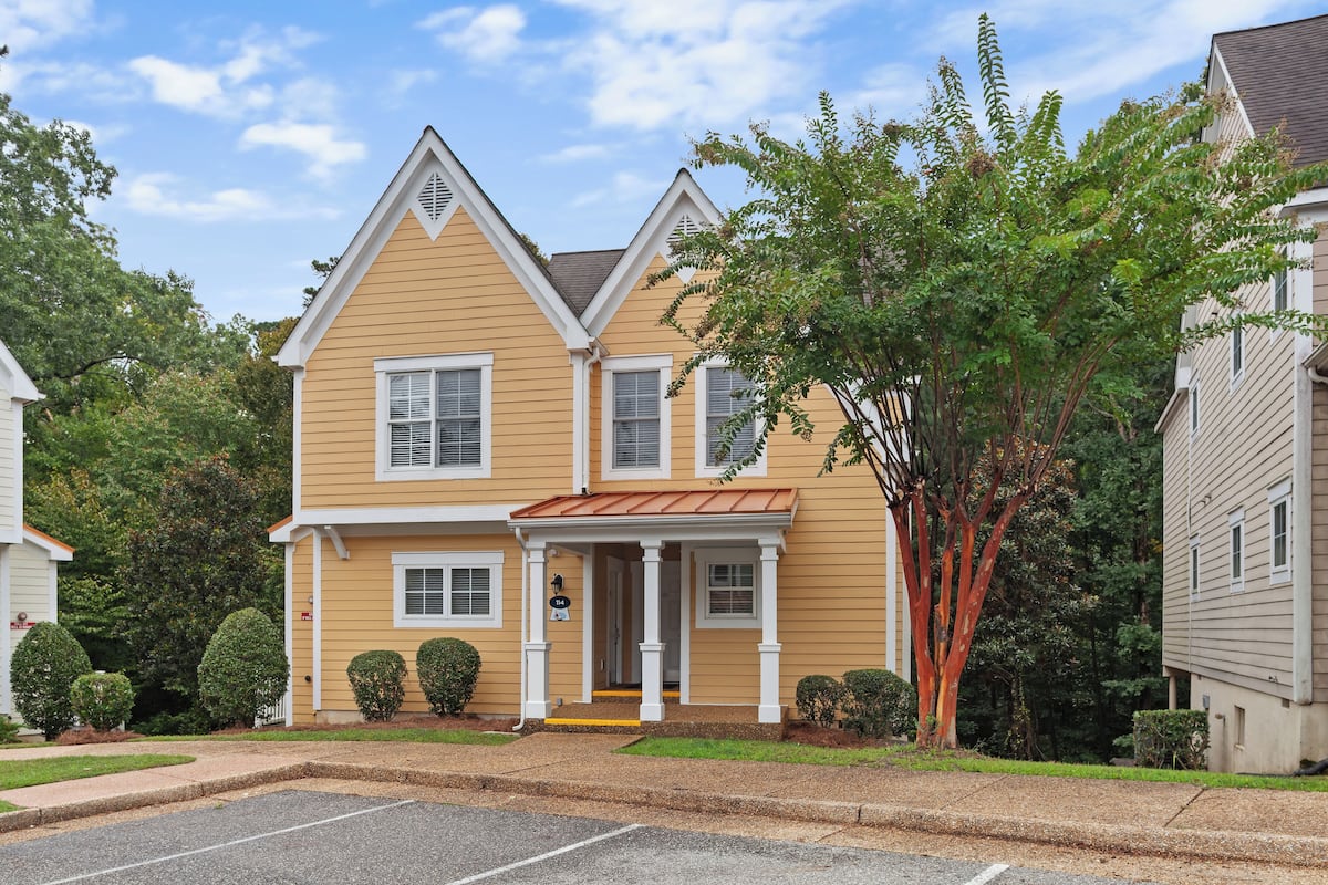 A two-story house with a front porch, a small garden, and a tree in front.