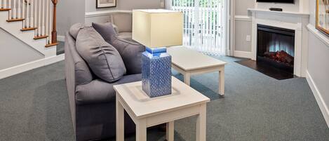 A living room with a grey sofa, a white coffee table with a blue vase, a fireplace, and a TV mounted above it.