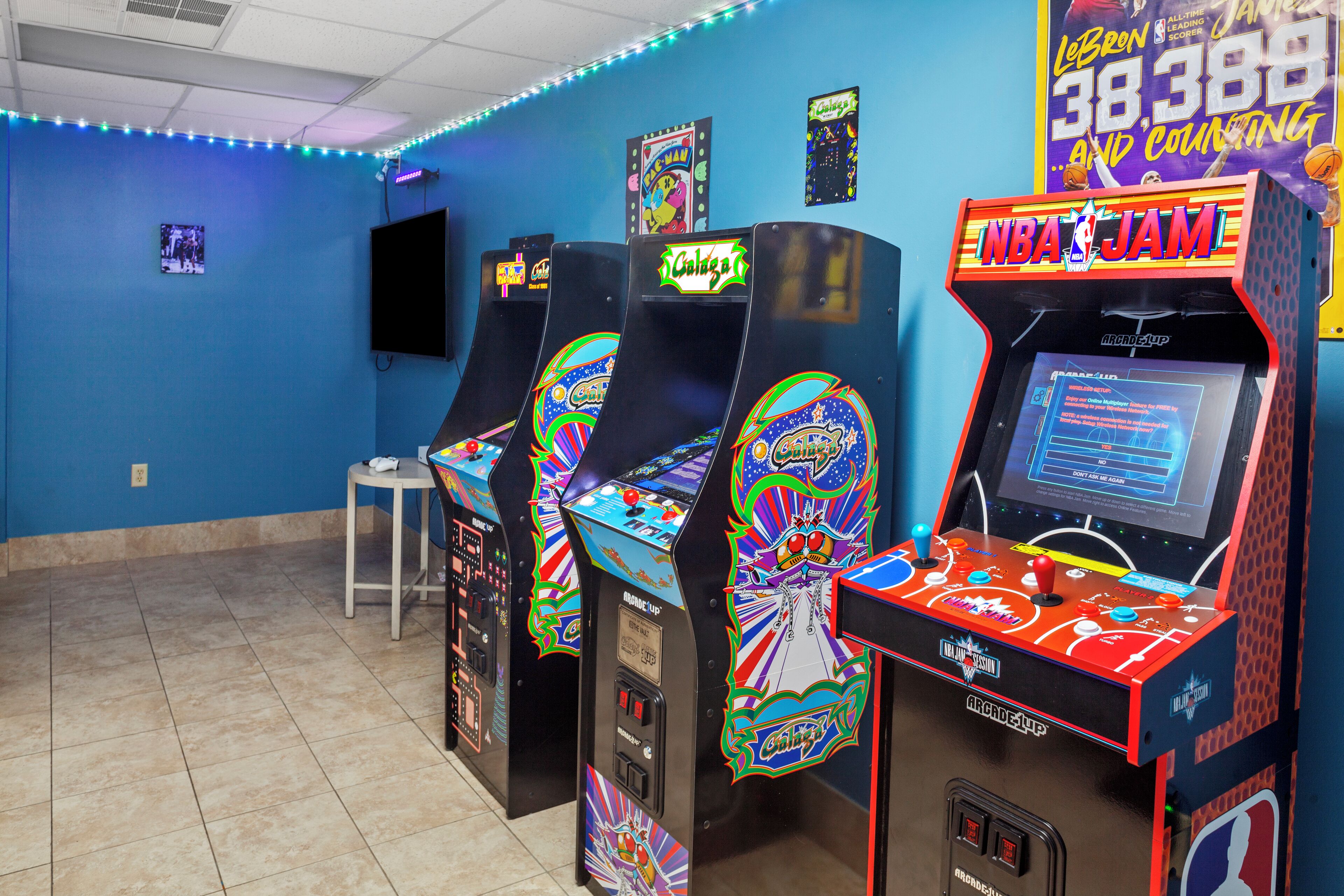 Una hilera de máquinas de videojuegos con diseños coloridos y una pared azul con carteles.