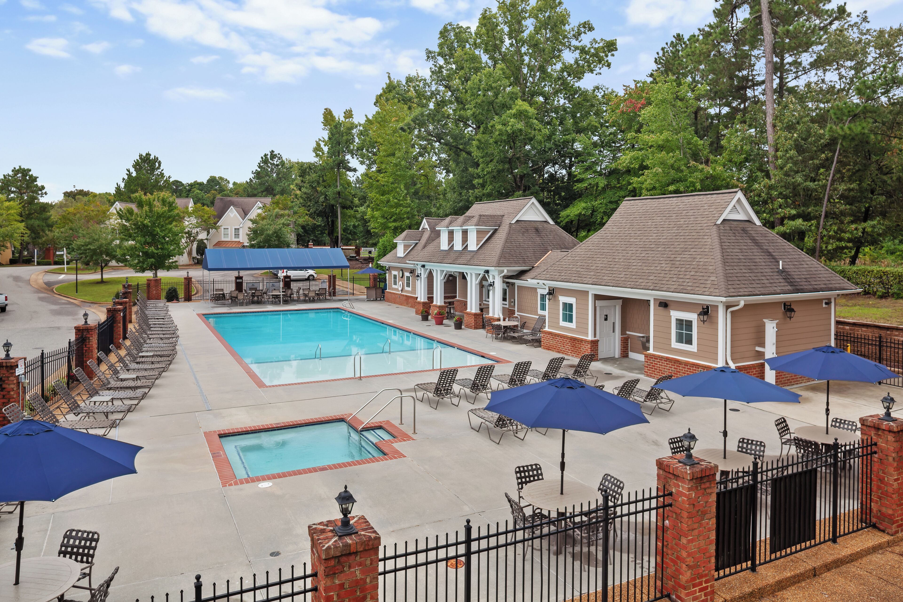A pool area with multiple lounge chairs and umbrellas, surrounded by brick buildings with a covered walkway.