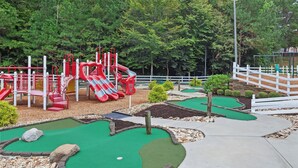 Un campo de minigolf con una estructura roja y blanca, rodeado por una cerca blanca y vegetación.