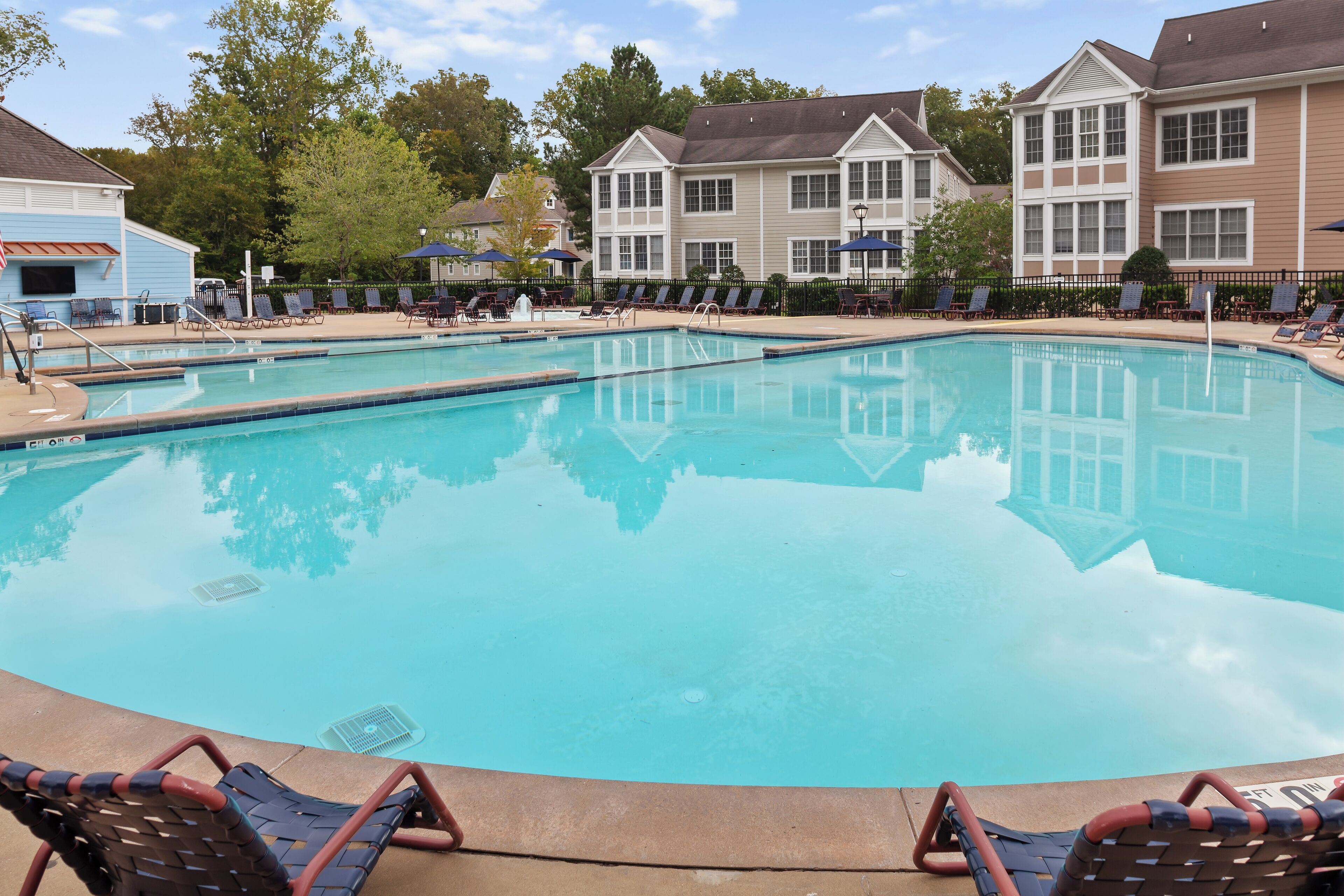 A swimming pool with lounge chairs and umbrellas, surrounded by buildings with large windows and a clear sky.