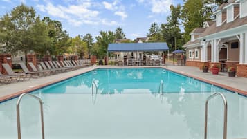A rectangular swimming pool with a tiled edge, surrounded by lounge chairs and a covered seating area.