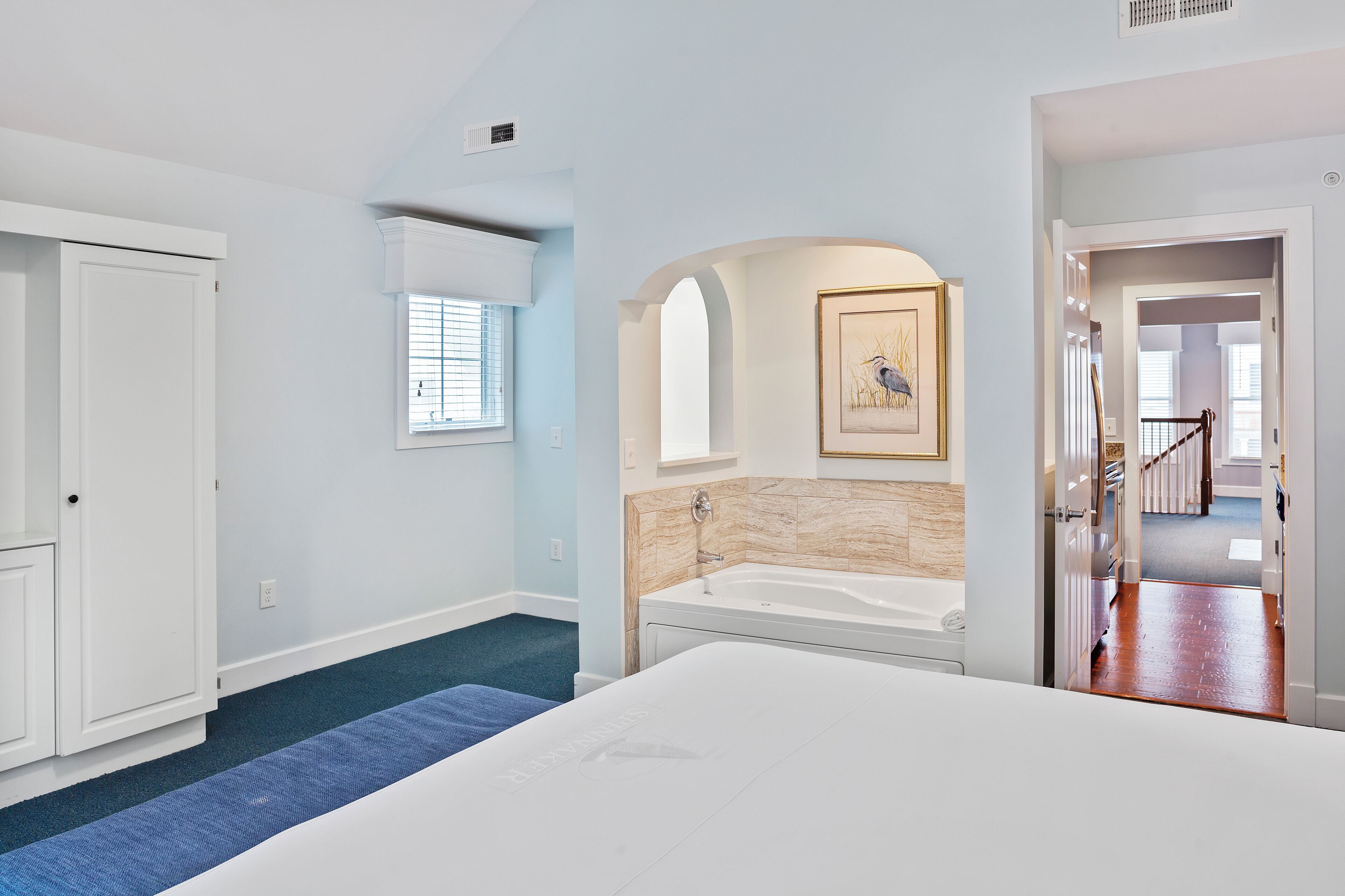 A bedroom with a large bed, a bathtub, and a window with blinds.