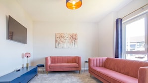 A modern living room with a large window, a blue cabinet, and two pink sofas. - Kessock View Apartment (Inverness)