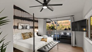 Un dormitorio moderno con una cama grande, una banca, un ventilador de techo y un balcón con vista a las montañas.