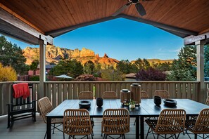 A covered patio with a wooden ceiling, a table set with plates and a vase, wicker chairs, and a view of red rock formations. - Uptown Sparks - Wow Views! 5BR 5BA, Pool, Spa, GamesRm, Walk into Uptown (Sedona)