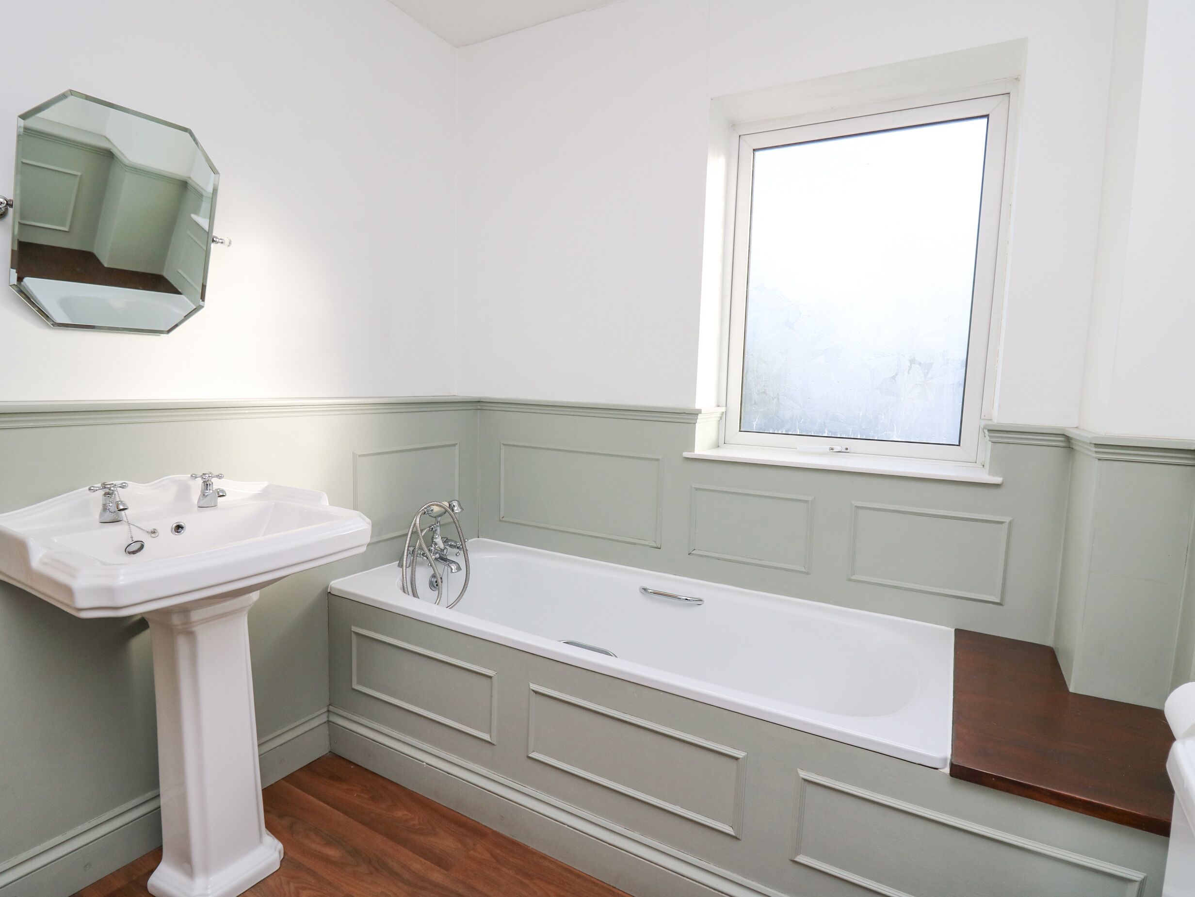 Un baño con un lavamanos blanco, una bañera y un ventanal.