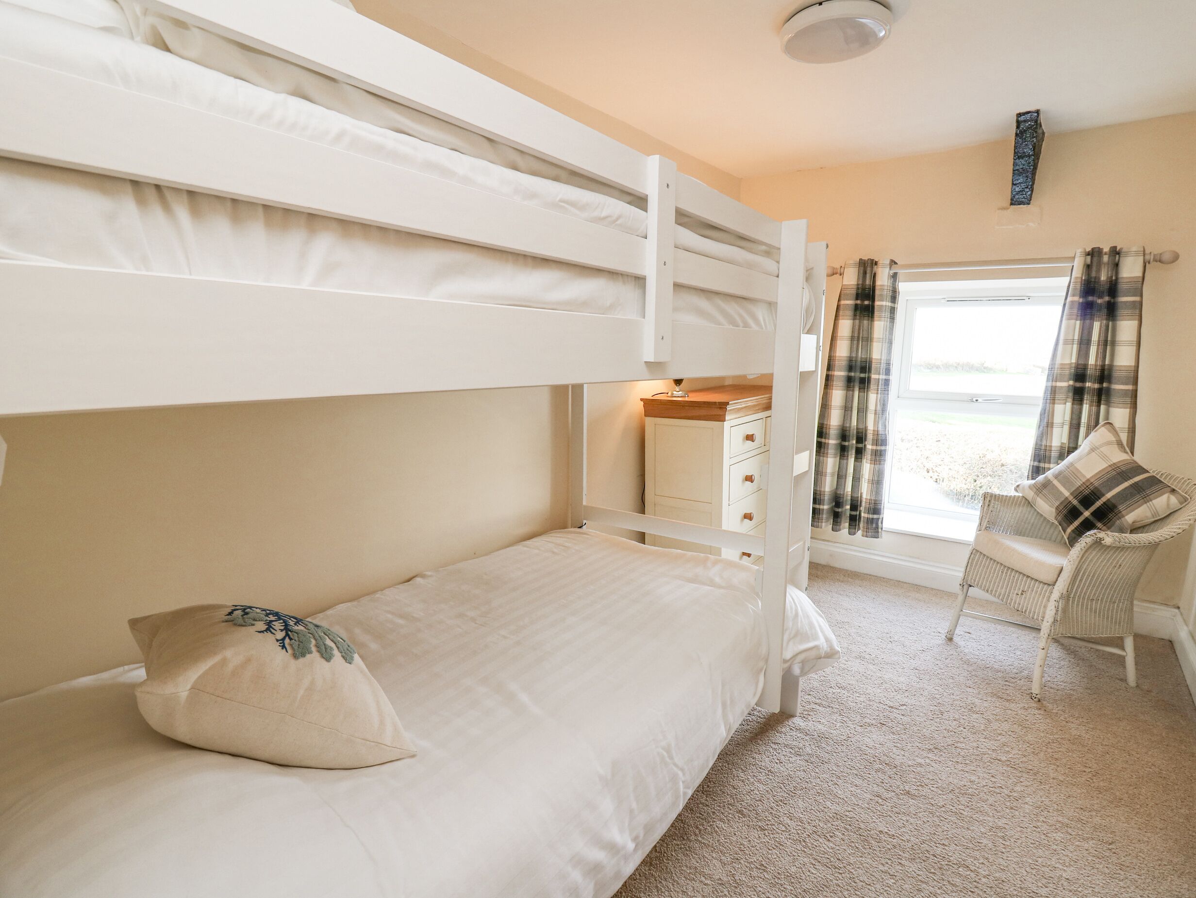 Een slaapkamer met een stapelbed, een klein bureau en stoel, een raam met gordijnen, en een vloerbedekking.