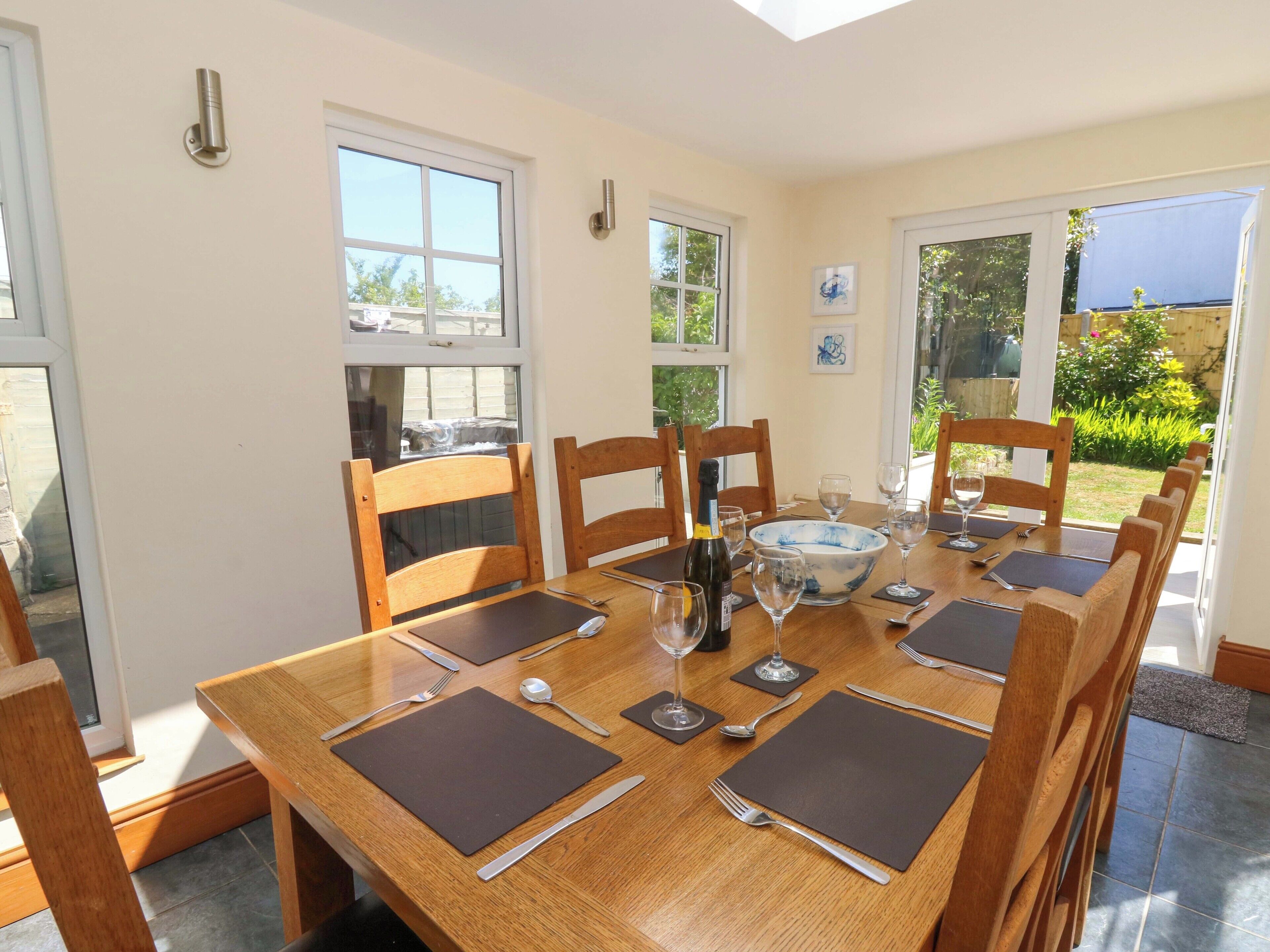 A dining area with a wooden table set for six, surrounded by wooden chairs.
