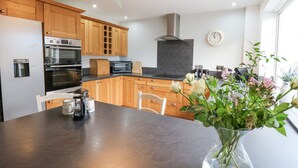 A modern kitchen with wooden cabinets, a black countertop, and a central island with a vase of flowers. - Towyn Hall (New Quay)