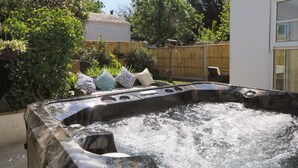 A hot tub in a backyard with a wooden fence, a chair, and decorative pillows. - Towyn Hall (New Quay)