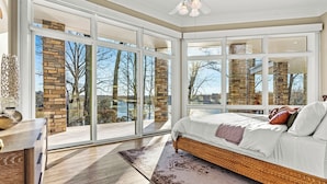 A bedroom with a large sliding glass door, a wicker bed, and a view of trees and a building. - Wake Up on Your Own Semi-Private Island - Lake Norman Retreat Sleeps 22 | Hot Tub, Private Covered Dock, 2 Game Rooms, Chef's Kitchen, Fire Pit, Kayaks, 2 Acres | Multi-Family & Group Getaways (Statesville)