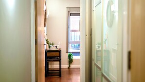 Un pasillo con piso de madera, una mesita con una planta y una ventana con persianas.