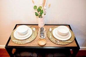 A dining table with two white plates, a clear glass, and a vase with green leaves and white flowers. - Stunning 1-bed Apartment in Sheffield City Centre (Sheffield)